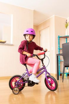 Little girl is riding a bicycle in her living room