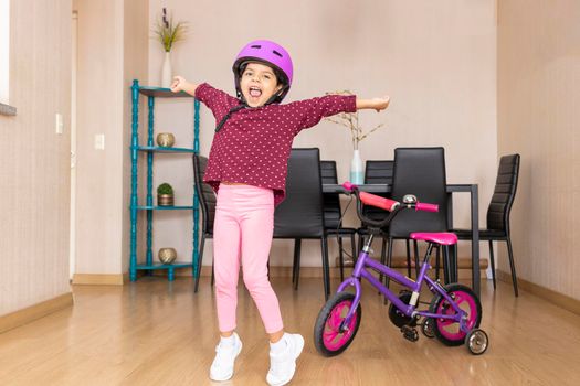 Little girl playing her bicycle in the living room of the apartment during quarantine