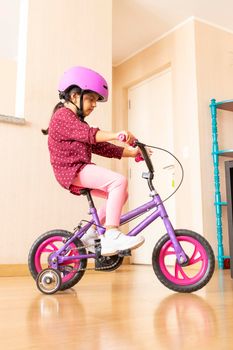 Little girl is riding a bicycle in her living room