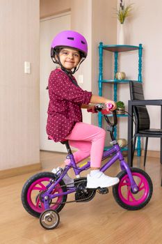 Little girl is riding a bicycle in her living room