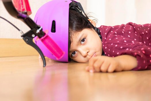 Sad little girl fell to the ground while playing with her bicycle in the house