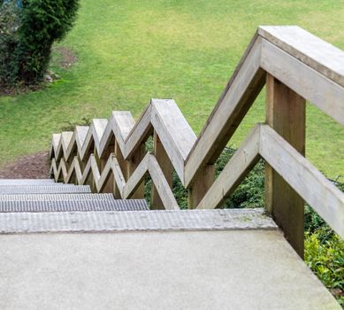 Zig-zag railings of wooden stairway on green grass background. A wooden stairs leading to a green lawn of outdoor landscape in Vancouver, Canada.