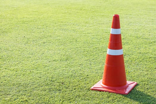 red plastic traffic cone on green grass field lawn with silver color reflective strip
