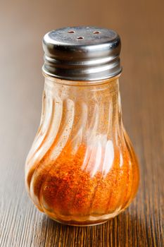 Close up ground chilli in glass bottle on wooden table, hot seasoning spice powdered ingredient for cooking