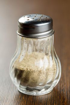 Close up ground white pepper in glass bottle on wooden table, hot seasoning spice powdered ingredient for cooking