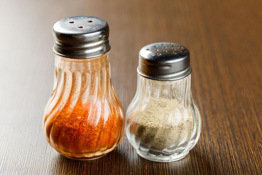 Close up ground chilli and pepper in glass bottle on wooden table, hot seasoning spice powdered ingredient for cooking