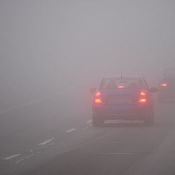 Cars in the fog. Bad winter weather and dangerous automobile traffic on the road. Light vehicles in fog.