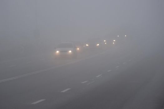 Cars in the fog. Bad winter weather and dangerous automobile traffic on the road. Light vehicles in fog.