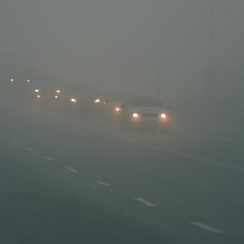 Cars in the fog. Bad winter weather and dangerous automobile traffic on the road. Light vehicles in fog.