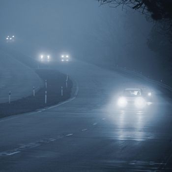 Cars in the fog. Bad winter weather and dangerous automobile traffic on the road. Light vehicles in fog.