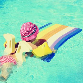 Little baby girl swims on the lilo in water at  hot sunny day. Summer holiday idyllic