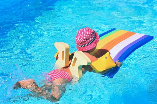 Little baby girl swims on the lilo in water at  hot sunny day. Summer holiday idyllic