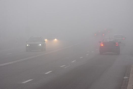 Cars in the fog. Bad winter weather and dangerous automobile traffic on the road. Light vehicles in fog.