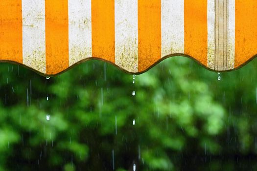 Rain. Awning on a balcony and drops of water on a natural colorful background during a spring day