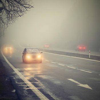 Cars in the fog. Bad winter weather and dangerous automobile traffic on the road. Light vehicles in foggy day.