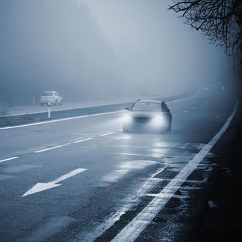 Cars in the fog. Bad winter weather and dangerous automobile traffic on the road. Light vehicles in foggy day.