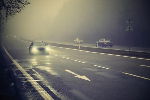 Cars in the fog. Bad winter weather and dangerous automobile traffic on the road. Light vehicles in foggy day.