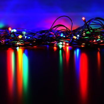 Christmas lights on black background with copy space. Colored reflecting surface.