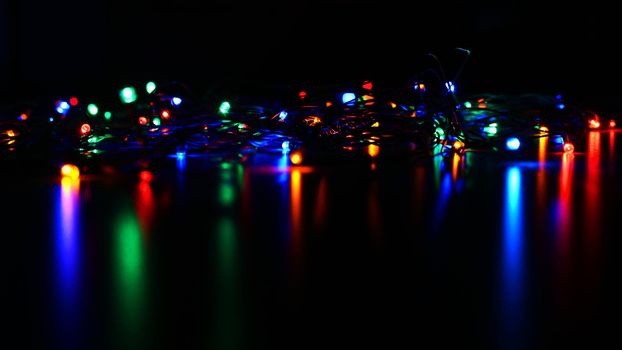 Christmas lights on black background with copy space. Colored reflecting surface.