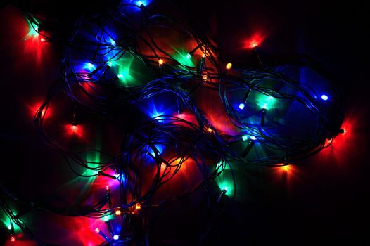 Christmas lights on black background with copy space. Colored reflecting surface.