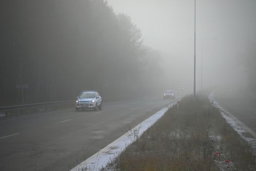 Cars in the fog. Bad winter weather and dangerous automobile traffic on the road. Light vehicles in foggy day.