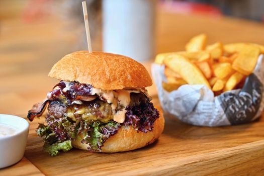 Delicious fresh homemade burger on a wooden table with sauce and French fries.