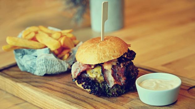 Delicious fresh homemade burger on a wooden table with sauce and French fries.