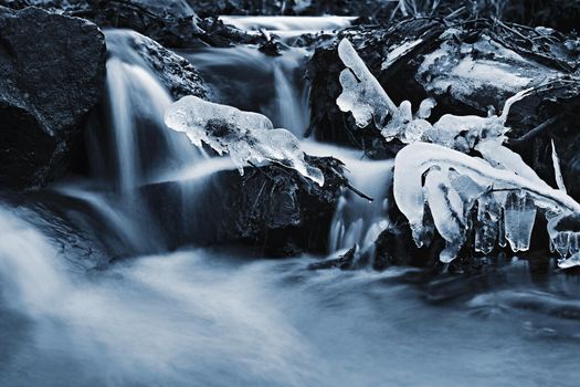 Blurred flowing water in winter creek. Beautiful photo of winter nature in the forest.