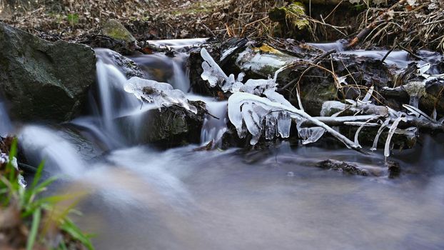 Blurred flowing water in winter creek. Beautiful photo of winter nature in the forest.