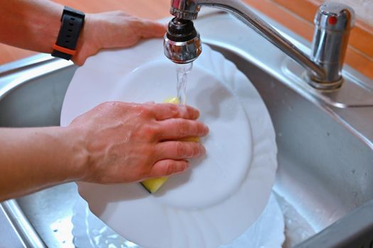Hand washing dishes. Hand with sponge and sink in kitchen washing dirty dishes - plate.