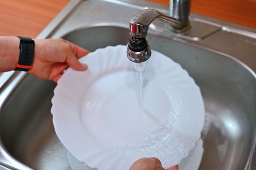 Hand washing dishes. Hand with sponge and sink in kitchen washing dirty dishes - plate.