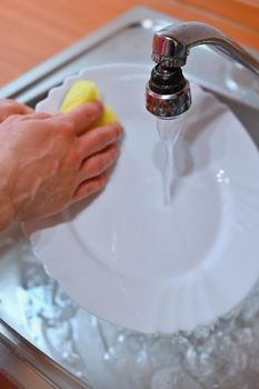 Hand washing dishes. Hand with sponge and sink in kitchen washing dirty dishes - plate.
