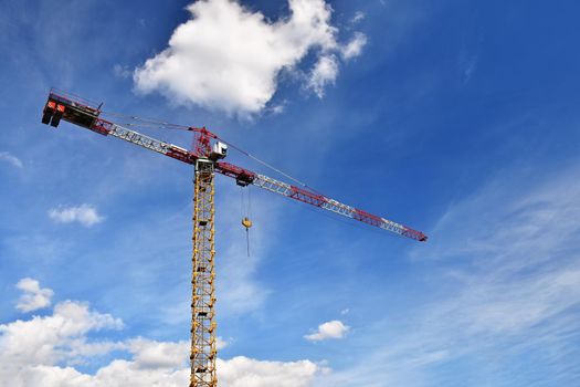 Crane on construction with blue sky clouds and sun in the background.