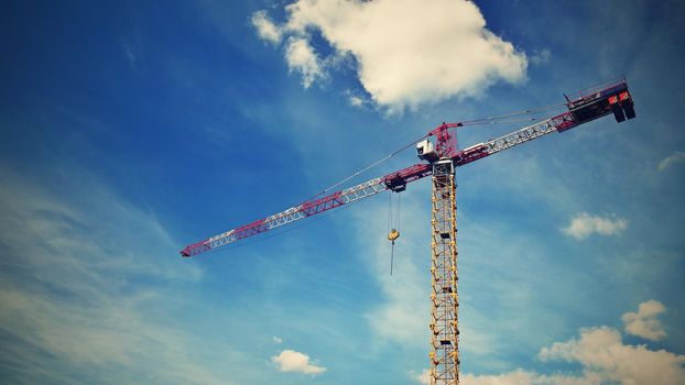 Crane on construction with blue sky clouds and sun in the background.