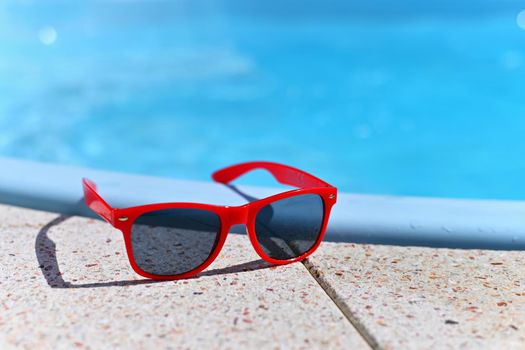 Summer background. Concept for summer and vacation. Red sunglasses by the pool in the background with blue water.