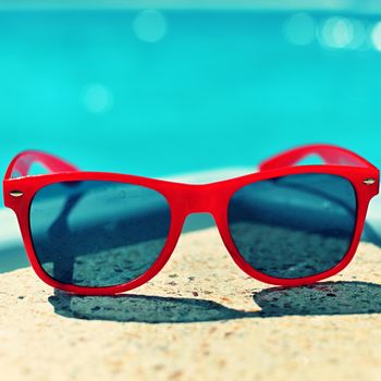 Summer background. Concept for summer and vacation. Red sunglasses by the pool in the background with blue water.