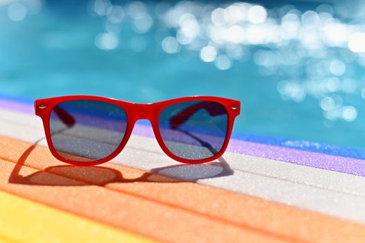 Summer background. Concept for summer and vacation. Red sunglasses by the pool in the background with blue water.