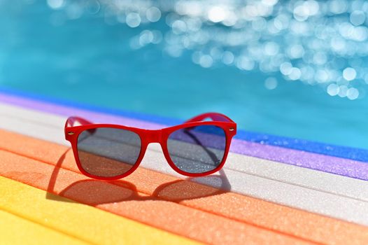 Summer background. Concept for summer and vacation. Red sunglasses by the pool in the background with blue water.