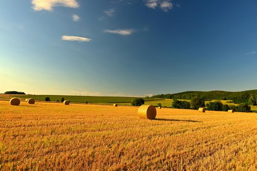 Hay bail harvesting in golden field landscape. Summer Farm Scenery with Haystack on the background of Beautiful Sunset.