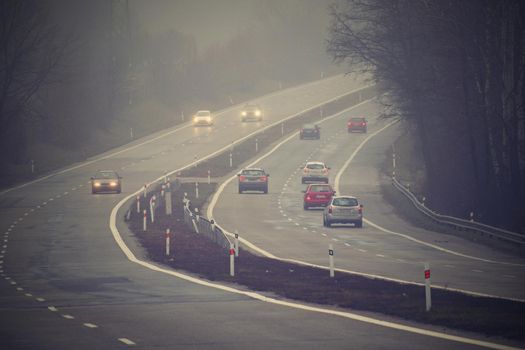 Cars in the fog. Bad winter weather and dangerous automobile traffic on the road. Light vehicles in foggy day.