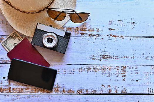 Items for summer vacation: a camera, passport,smartphone, money, hat, sunglasses. Wooden background, top view with Copy space. Beautiful summer concept for travel and summer vacation-holidays.