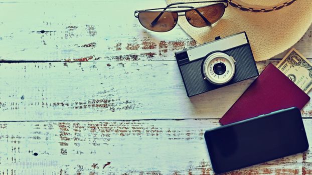 Items for summer vacation: a camera, passport,smartphone, money, hat, sunglasses. Wooden background, top view with Copy space. Beautiful summer concept for travel and summer vacation.