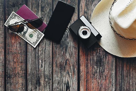 Items for summer vacation: a camera, passport,smartphone, money, hat, sunglasses. Wooden background, top view with Copy space. Beautiful summer concept for travel and summer vacation.