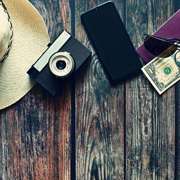 Items for summer vacation: a camera, passport,smartphone, money, hat, sunglasses. Wooden background, top view with Copy space. Beautiful summer concept for travel and summer vacation.