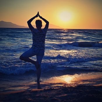 Woman meditates - relaxes at sunset by the sea on the beach. Concept for yoga, health and spa.