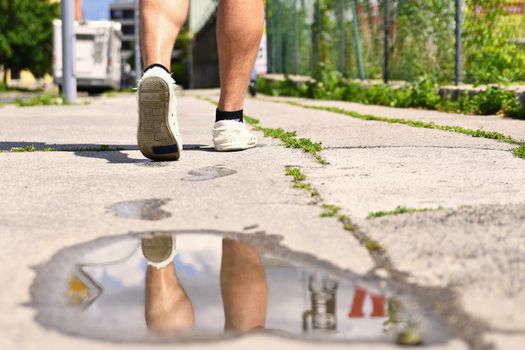 Legs while walking. Reflections in water on the sidewalk.