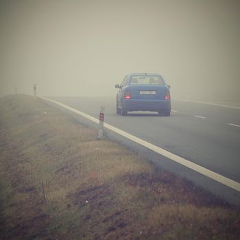 Car on the road in the fog. Autumn landscape - dangerous road traffic in winter season.