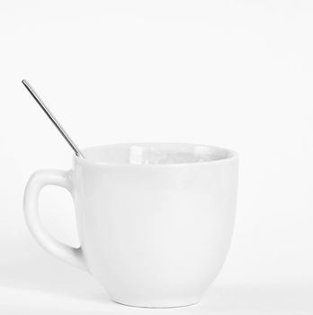 A small white cup of coffee with a spoon. Isolated on a clean white background.