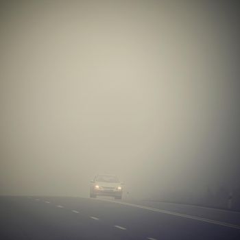 Car on the road in the fog. Autumn landscape - dangerous road traffic in winter season.