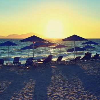 Sunbeds and umbrella on the beach at sunset by the sea. Beautiful concept for vacation, summer holidays and travel.